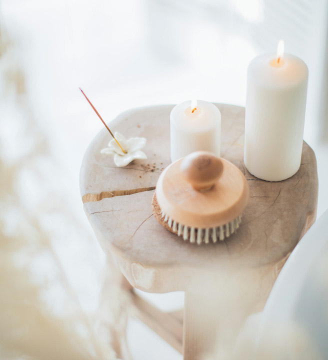 Lit candles, a dry brush, & burning incense on a wooden stool